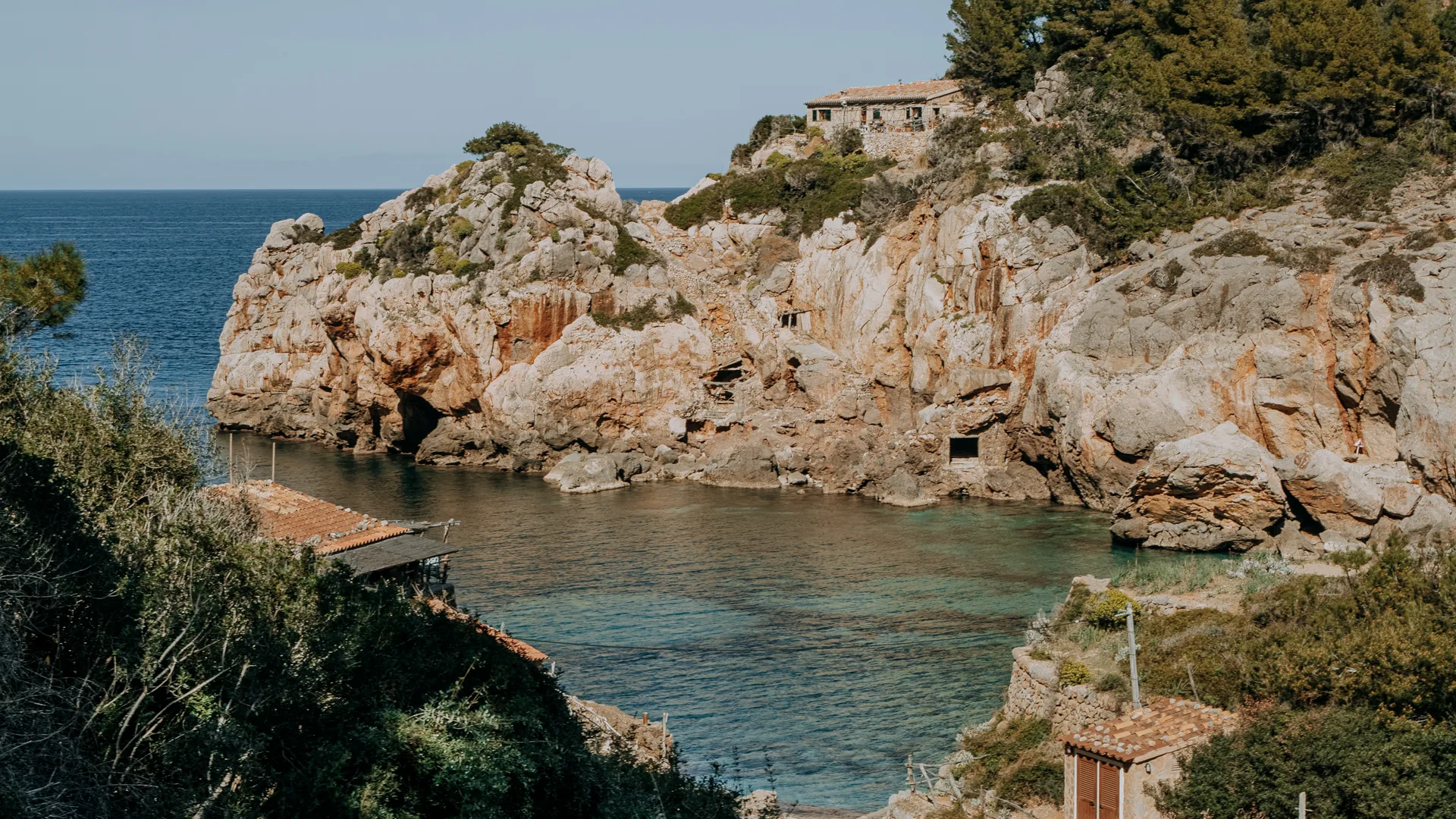 Knight Frank auf Mallorca: Felsbucht mit Bootshäusern und einem Natursteinhaus über dem Meer