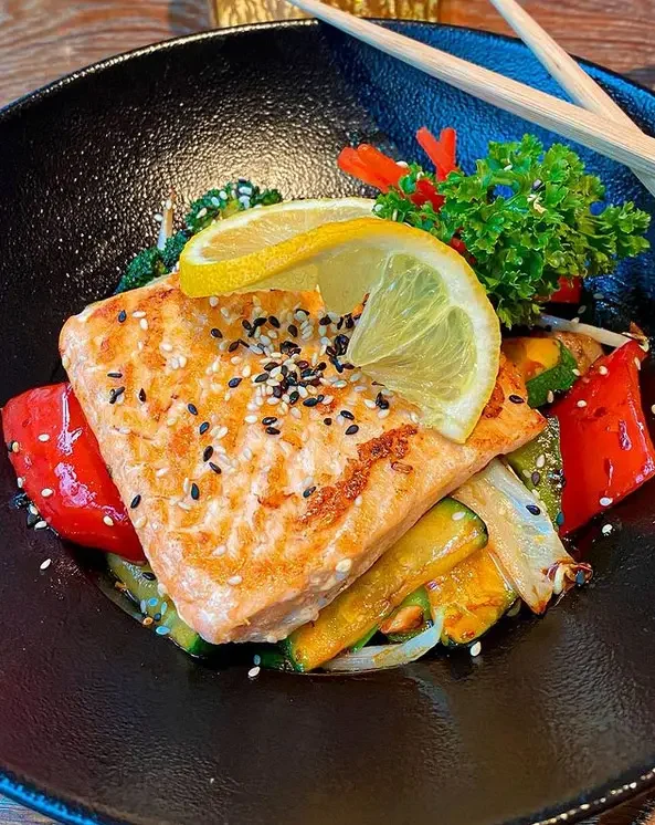 Gebratener Lachs auf Wokgemüse in einer schwarzen Schale